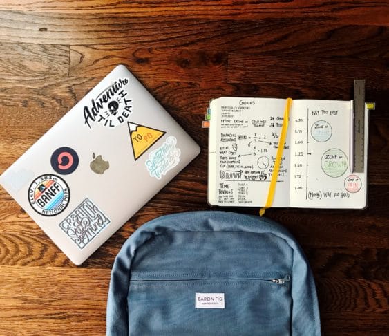 Image of a backpack, notebook, and laptop on a wooden desk