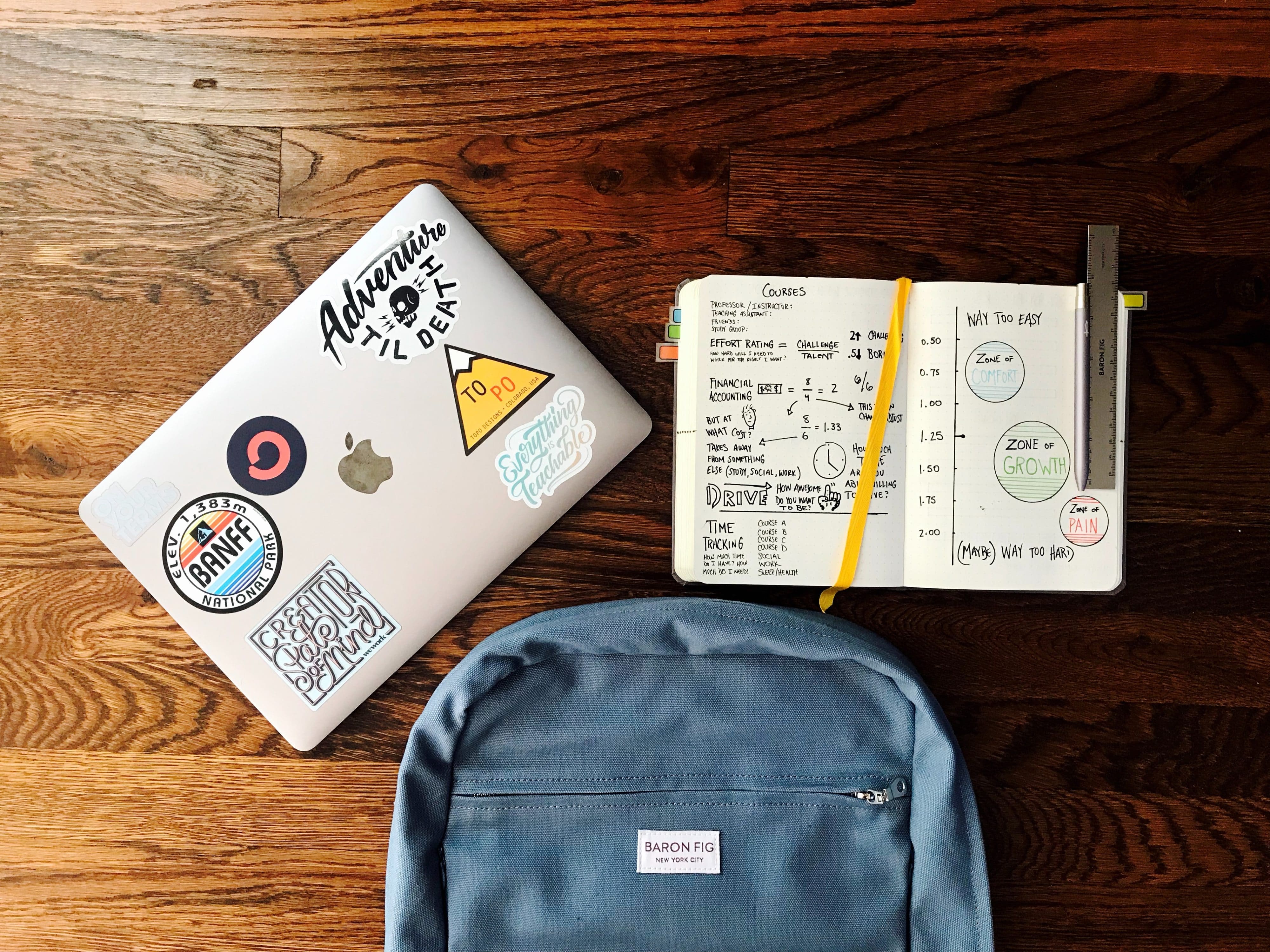 Image of a backpack, notebook, and laptop on a wooden desk