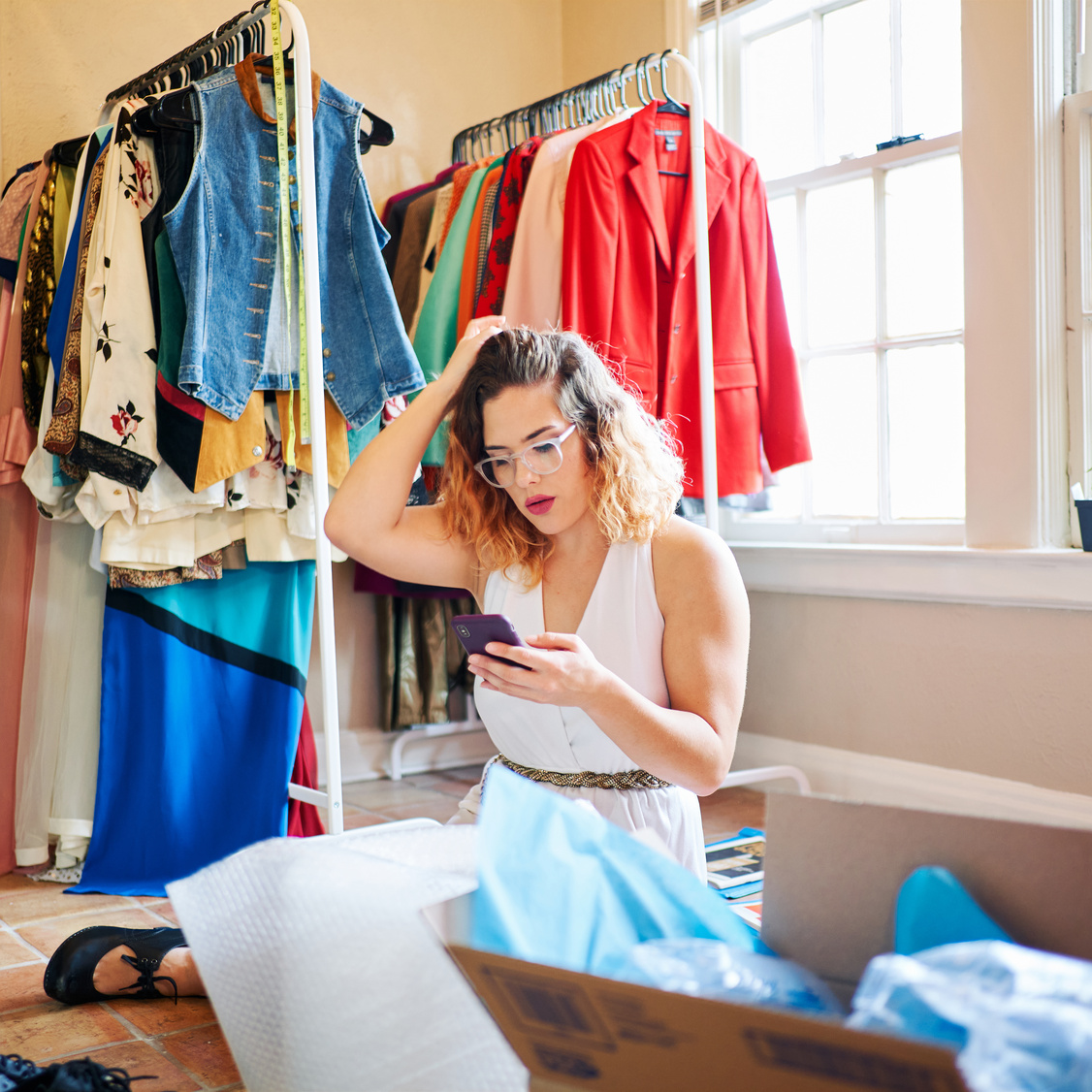 Seller checking their phone with clothes on a rack in the background